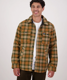 A man wearing a brown and tan plaid overshirt over a white t-shirt and dark pants, standing against a light gray studio background.